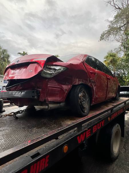 A red sedan on a rollback tow truck in Coral Springs.